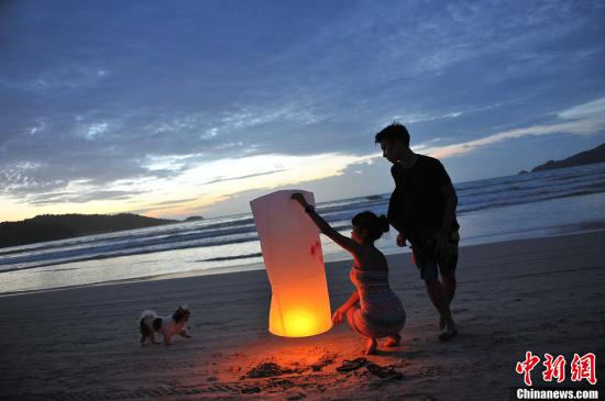 普吉岛被誉为泰国的“珍珠”，这里拥有迷人的风光和丰富的旅游资源，每年都吸引众多游客来此休闲观光。图为两名游客在燃放孔明灯。洪坚鹏 摄